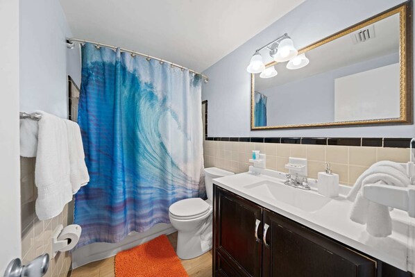Un baño con cortina de ducha, inodoro, lavamanos y espejo.