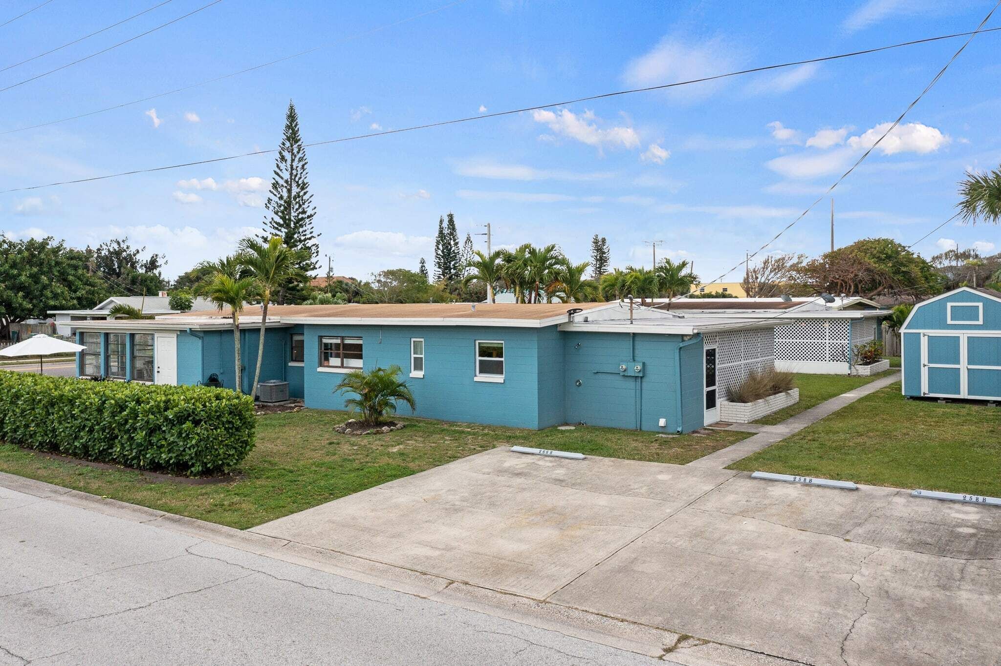 A single-story blue house with a small attached garage, a front yard with a hedge, and a clear sky.