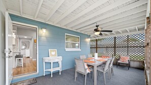 A covered patio with a dining table and chairs, a ceiling fan, and a view through a lattice fence. - Midtown Cottage - Walk to it All! (Cocoa Beach)