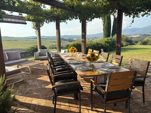 Un espace de restauration en plein air avec vue sur la campagne, agrémenté d’une pergola et d’une table dressée pour quatre personnes.