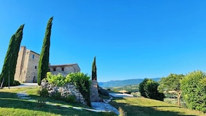 A stone building with a tower, surrounded by well-maintained greenery and a clear blue sky. - 360° views, pool, AC, pizza oven & bocce court (Casigliano, Acquasparta)