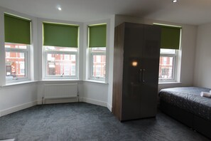 Een slaapkamer met een grote kast, een bed en drie ramen voorzien van groene jaloezieën.