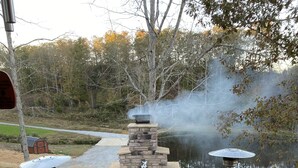 A stone fireplace with a chimney, surrounded by a wooden deck with chairs and a grill. - Remote Cabin with all amenities  (Lutts)