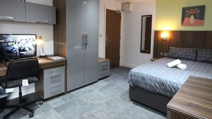 A hotel room with a bed, desk, wardrobe, and a television.
