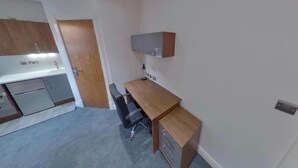 A compact room with a kitchenette, a wooden desk, a chair, and a small cabinet.
