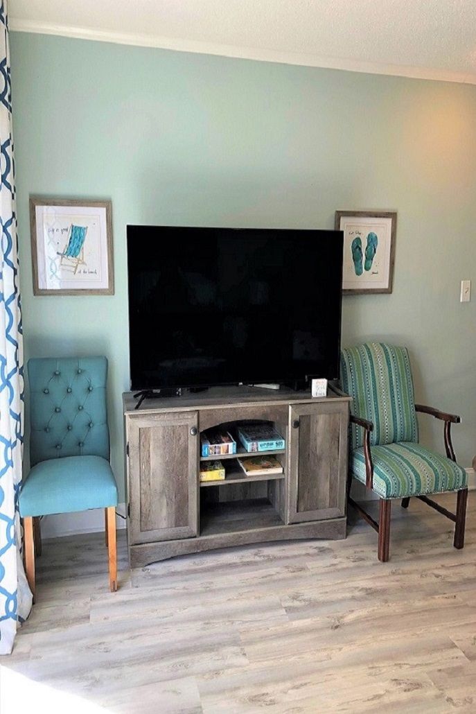 A living room with a flat-screen TV on a wooden stand, two chairs, and framed artwork on the walls.