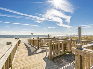 Una pasarela de madera que lleva a una playa con cielo despejado y el sol brillando.