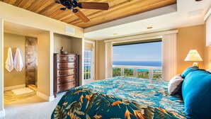 A bedroom with a large bed, a dresser, a ceiling fan, and a view of the ocean. - Coastline View (Kailua-Kona)