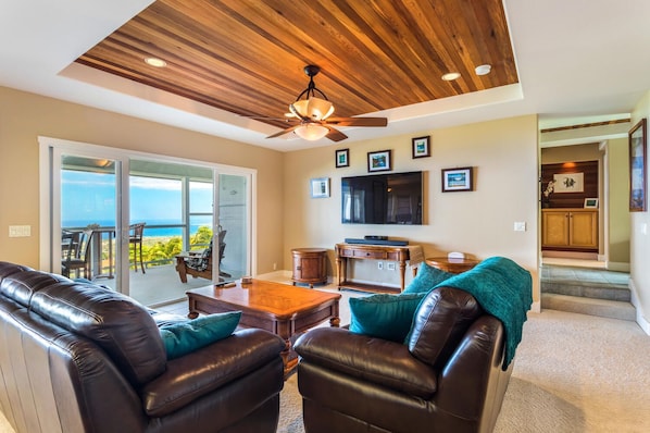 A living room with leather sofas, a wooden coffee table, a ceiling fan, and a TV on the wall.
