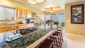 A modern kitchen with a large island, wooden cabinets, and a view of the ocean. - Coastline View (Kailua-Kona)