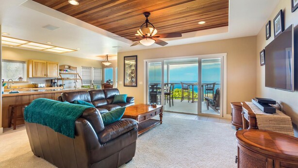 A spacious living room with a leather sofa, a wooden coffee table, and a view of the ocean through large sliding glass doors. - Coastline View (Kailua-Kona)