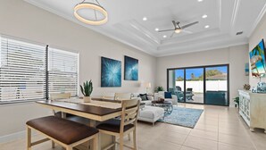 A modern living room with a dining area, large windows, ceiling fans, and a view of the outdoors. - LimitedTime Special Offer  New Vanderbilt Beach Home Heated Saltwater Pool & Spa (Naples)