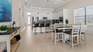 A modern kitchen with white cabinets, stainless steel appliances, and a dining area with a wooden table and chairs. - LimitedTime Special Offer  New Vanderbilt Beach Home Heated Saltwater Pool & Spa (Naples)