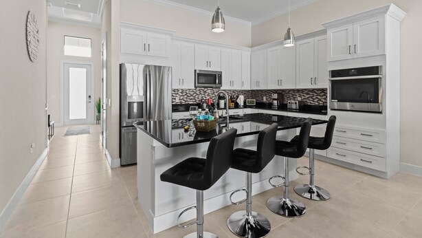 A modern kitchen with white cabinets, stainless steel appliances, a central island with bar stools, and pendant lighting. - LimitedTime Special Offer  New Vanderbilt Beach Home Heated Saltwater Pool & Spa (Naples)