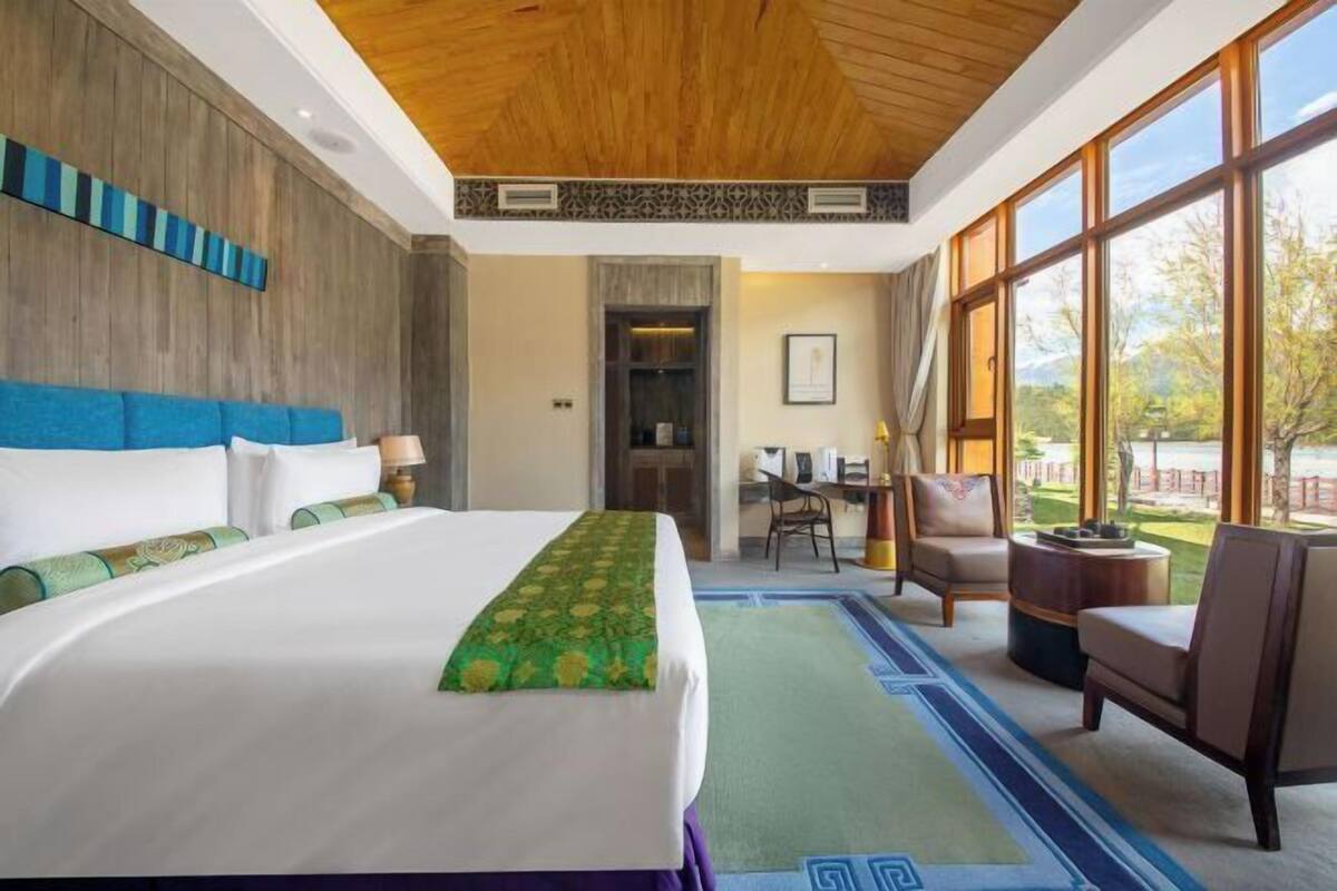 A hotel room with a large bed, a desk, two chairs, and a view of the outdoors.