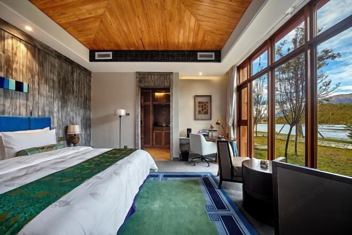 A hotel room with a large bed, a desk, and a view of a lake.