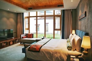 Habitación de hotel con una cama grande, televisor, sofá y ventana con vistas a la arquitectura tradicional.