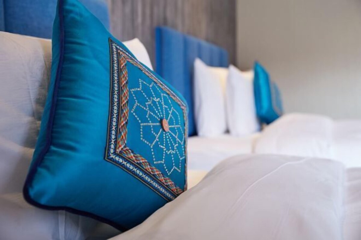 A bed with white bedding and a blue pillow with a geometric pattern.
