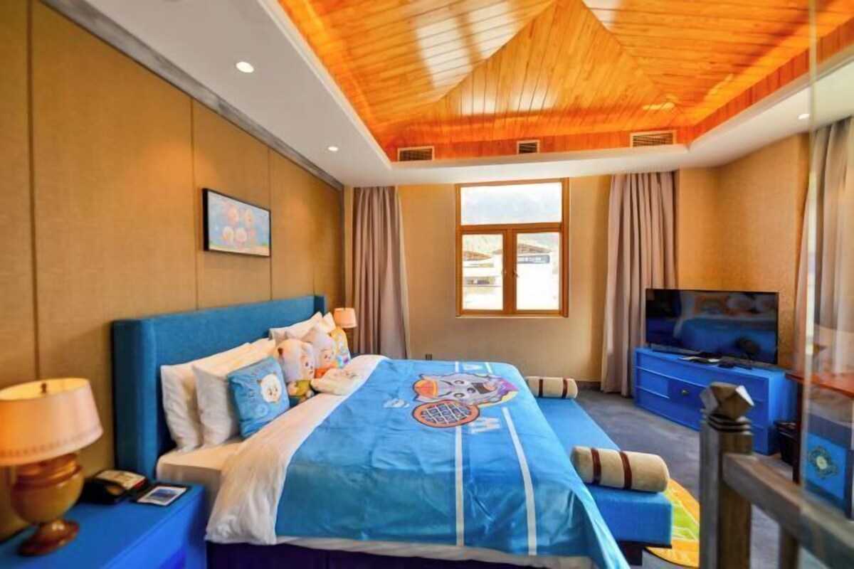 A hotel room with a large bed, a television, a desk with a lamp, and a window with curtains.