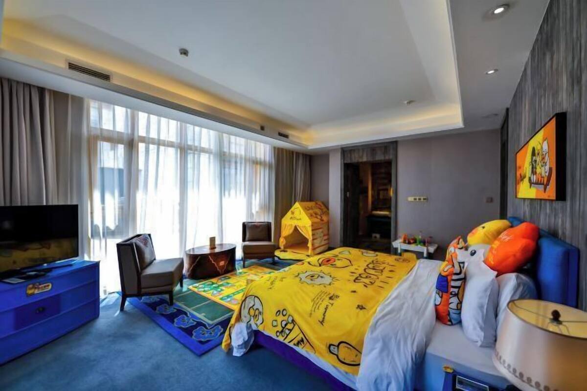 A hotel room with a large bed, a TV, a desk, and a window with curtains.