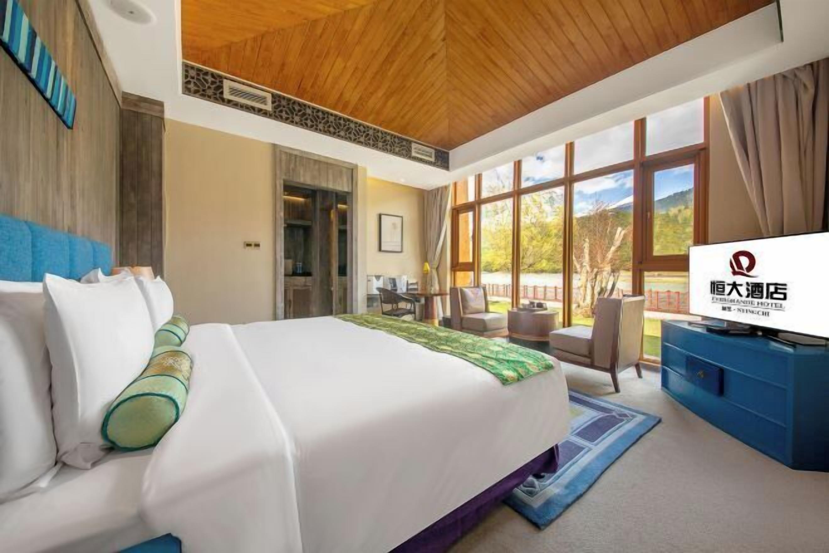 A hotel room with a large bed, a TV, a desk, and a view of the outdoors.