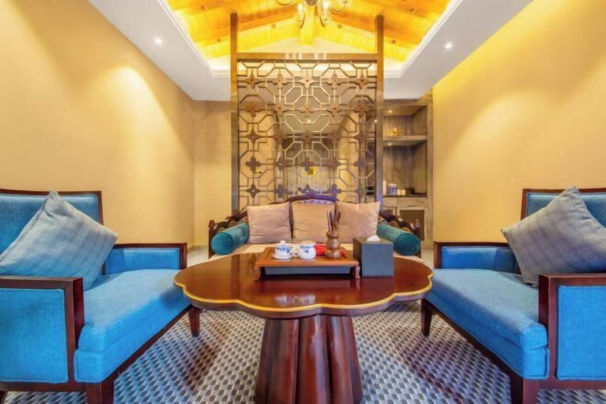 A room with a round wooden coffee table, two blue sofas, a decorative partition, and a ceiling with a chandelier.