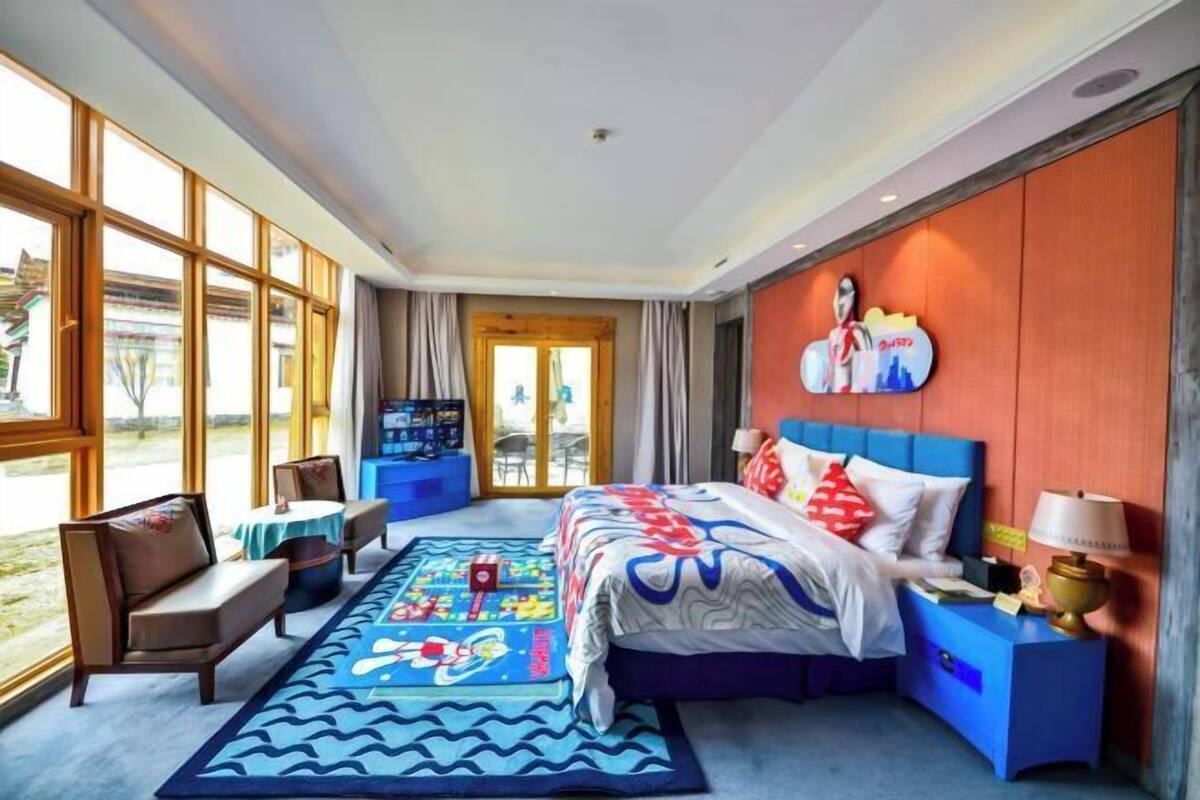 A hotel room with a large bed, a blue headboard, a nightstand, a desk, a chair, and a window with a view of the outdoors.