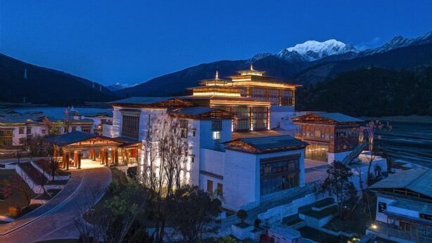 A traditional building with multiple levels and a prominent central structure, surrounded by smaller buildings and a mountainous backdrop. - Evergrande Hotel, Nyingchi (Nyingchi)