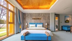 A large bed with a blue headboard, a wooden ceiling, and a view of the outdoors through large windows. - Evergrande Hotel, Nyingchi (Nyingchi)