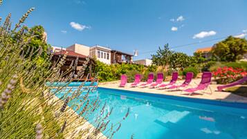 A swimming pool with pink lounge chairs and a building in the background.