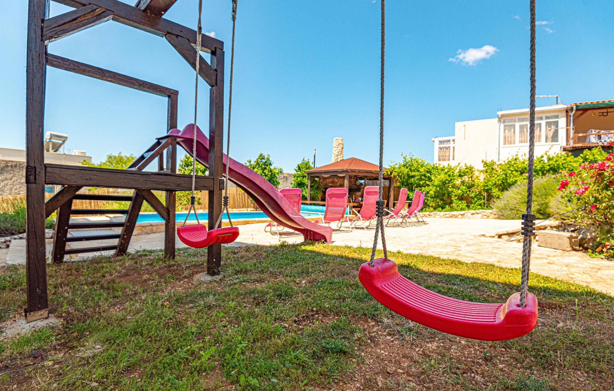 A playground with swings and a slide, a pool, and a gazebo in a backyard.