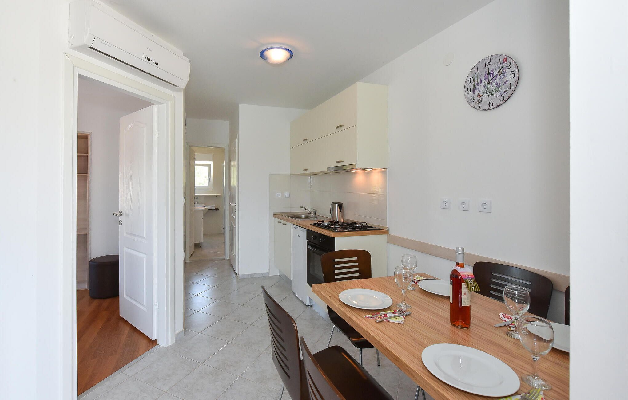 A modern kitchen with white cabinets, a wooden dining table set with plates and glasses, and a wall clock.