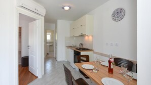 A modern kitchen with white cabinets, a wooden dining table set with plates and glasses, and a wall clock. - Stunning home in Rogoznica (Rogoznica)