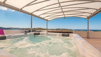 A hot tub under a canopy with a view of the sea and hills.