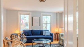 A living room with a blue sofa, wicker chairs, a glass coffee table, and a patterned rug. - Classic Mystic Retreat Walking Distance to Downtown (Groton)