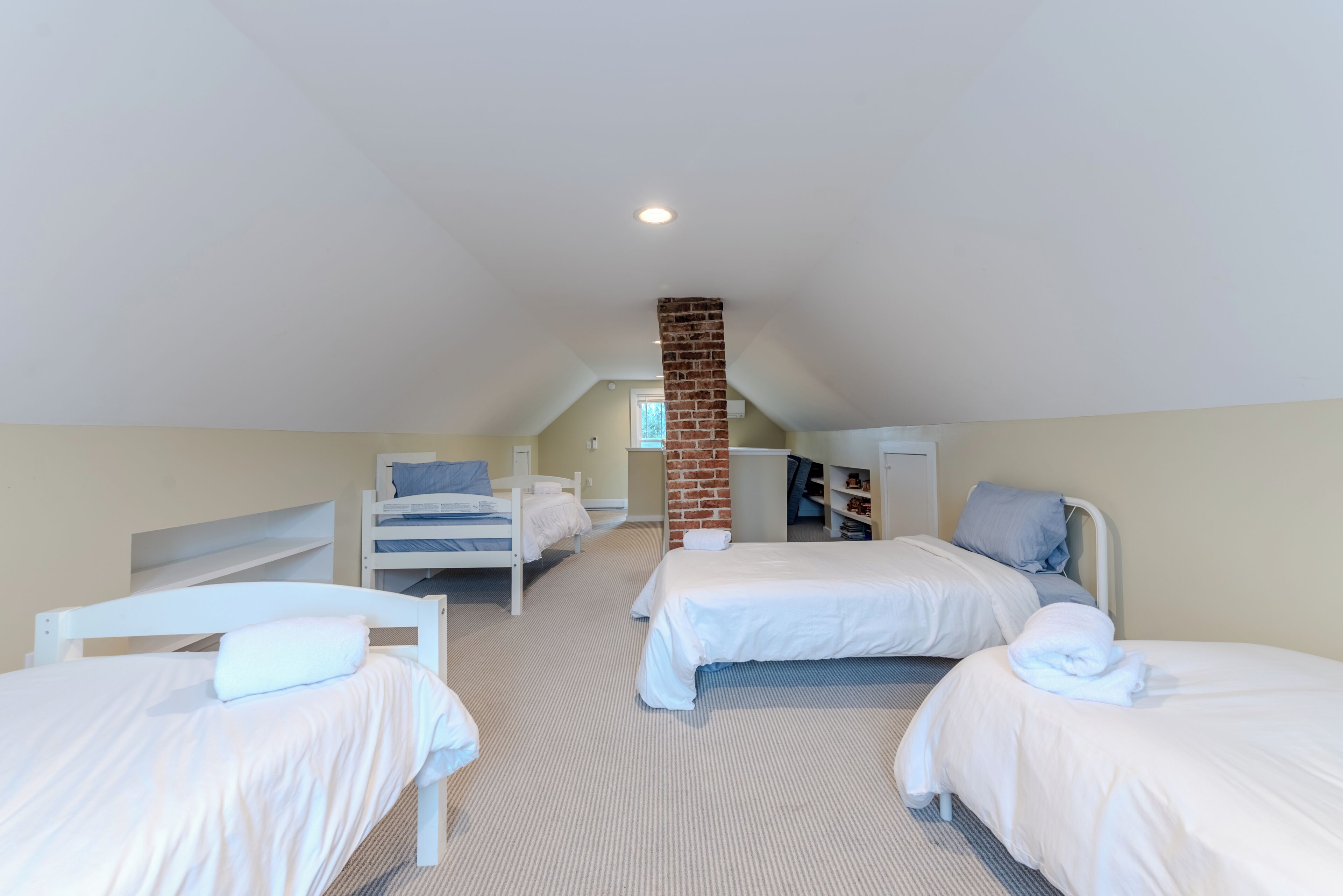 A room with two beds, a brick chimney, and a white ceiling.