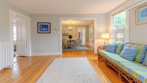 A spacious living room with a wooden floor, a sofa with striped cushions, a dining area with a table and chairs, and a framed picture on the wall. - Classic Mystic Retreat Walking Distance to Downtown (Groton)