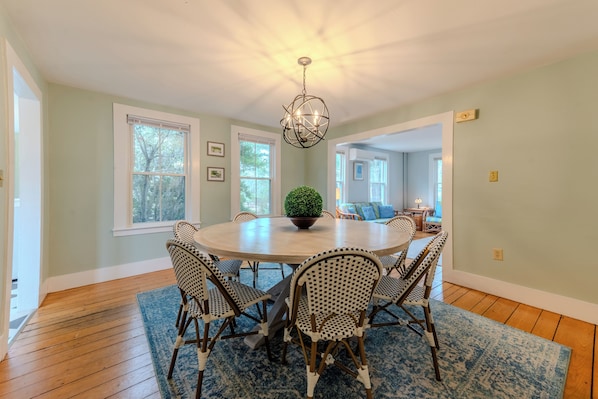A dining room with a round table, six chairs, a chandelier, and a potted plant.