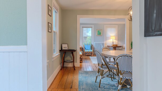 A hallway leading to a dining area with a table and chairs, framed pictures on the wall, and a lamp on a side table. - Classic Mystic Retreat Walking Distance to Downtown (Groton)