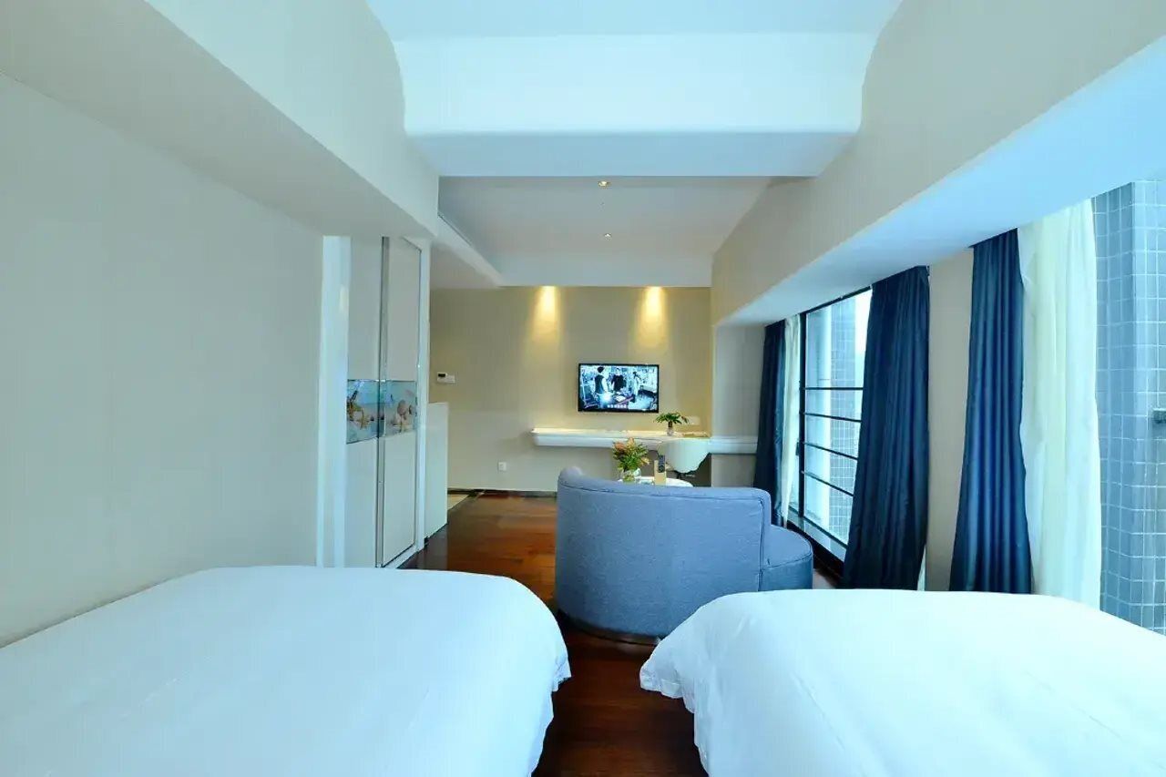 Ein Hotelzimmer mit zwei Betten, einer kleinen Sitzecke, einem Fernseher und einem Fenster mit Vorhängen.