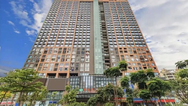 A tall, modern high-rise building with a central glass facade and multiple balconies. - Vienna Apartment (Shenzhen)