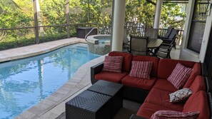 A pool area with a red sofa and black woven ottoman, surrounded by chairs and a hot tub. - Serene Waterfront Home, walk to TigerTail Beach, Pet Friendly, EV Charger (Marco Island)
