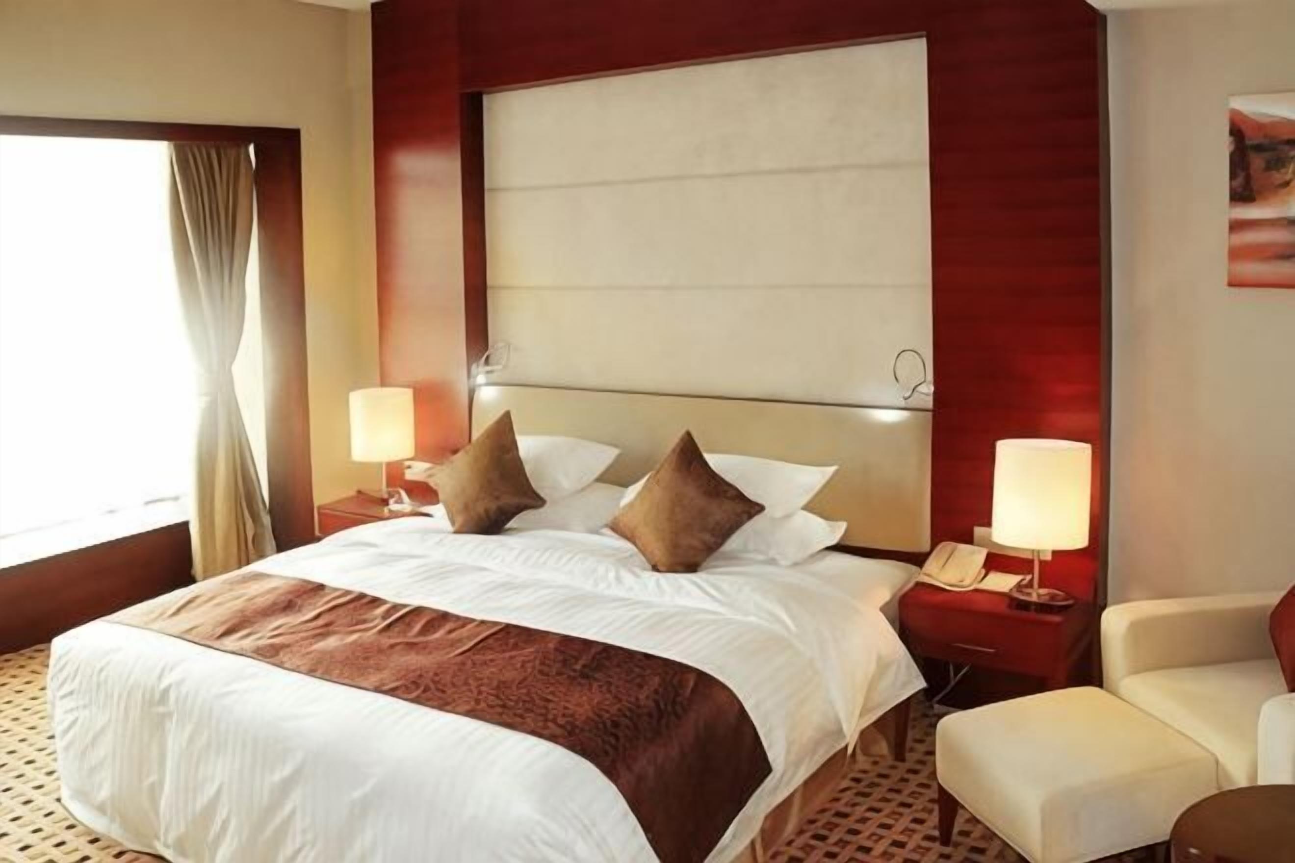 Een hotelkamer met een groot bed, twee nachtkastjes met lampen, een stoel en een raam met gordijnen.