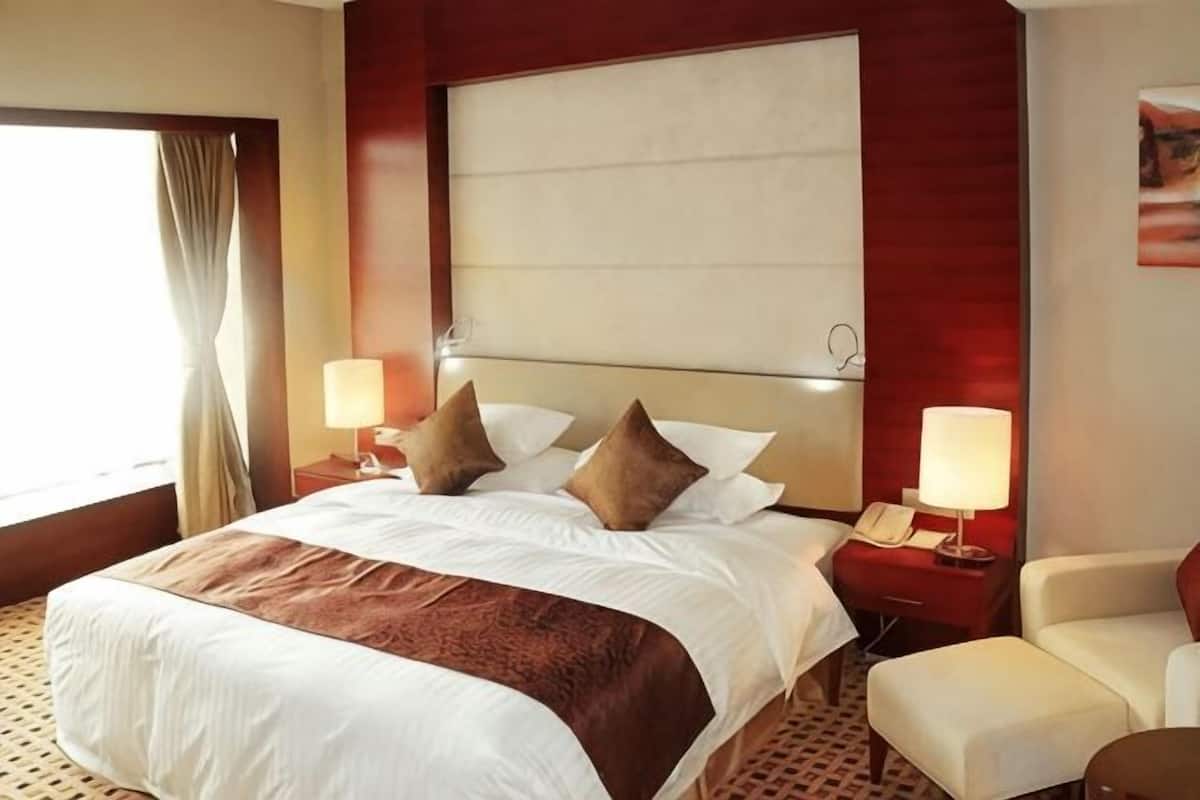 Ett hotellrum med en stor säng, två sängbord med lampor, en stol och ett fönster med gardiner.