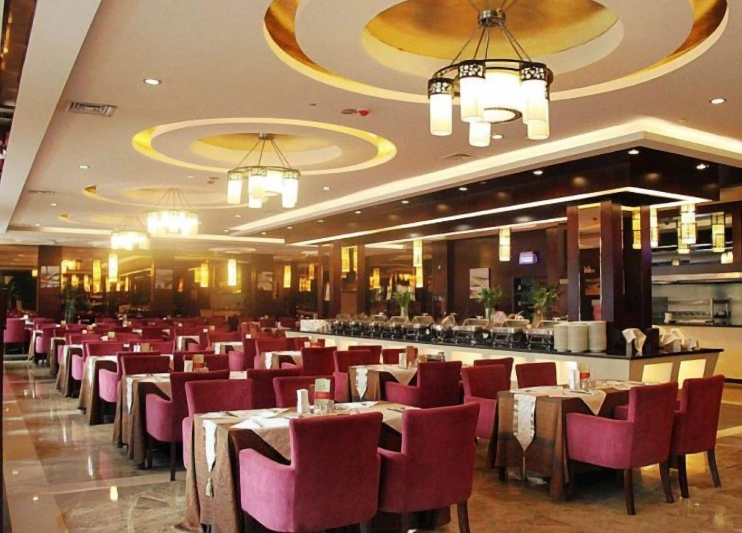 A spacious restaurant with multiple dining tables and chairs, a bar area, and modern lighting fixtures.