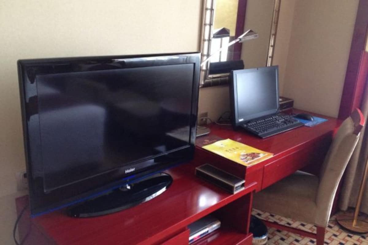 Habitación de hotel con una televisión de pantalla plana grande, una computadora portátil y un escritorio con una silla.
