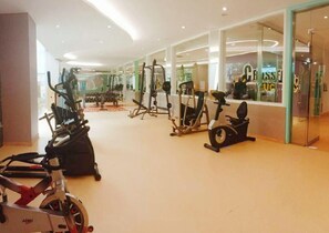 Een sportschool met diverse fitnessapparaten, waaronder loopbanden, hometrainers en krachtapparaten.