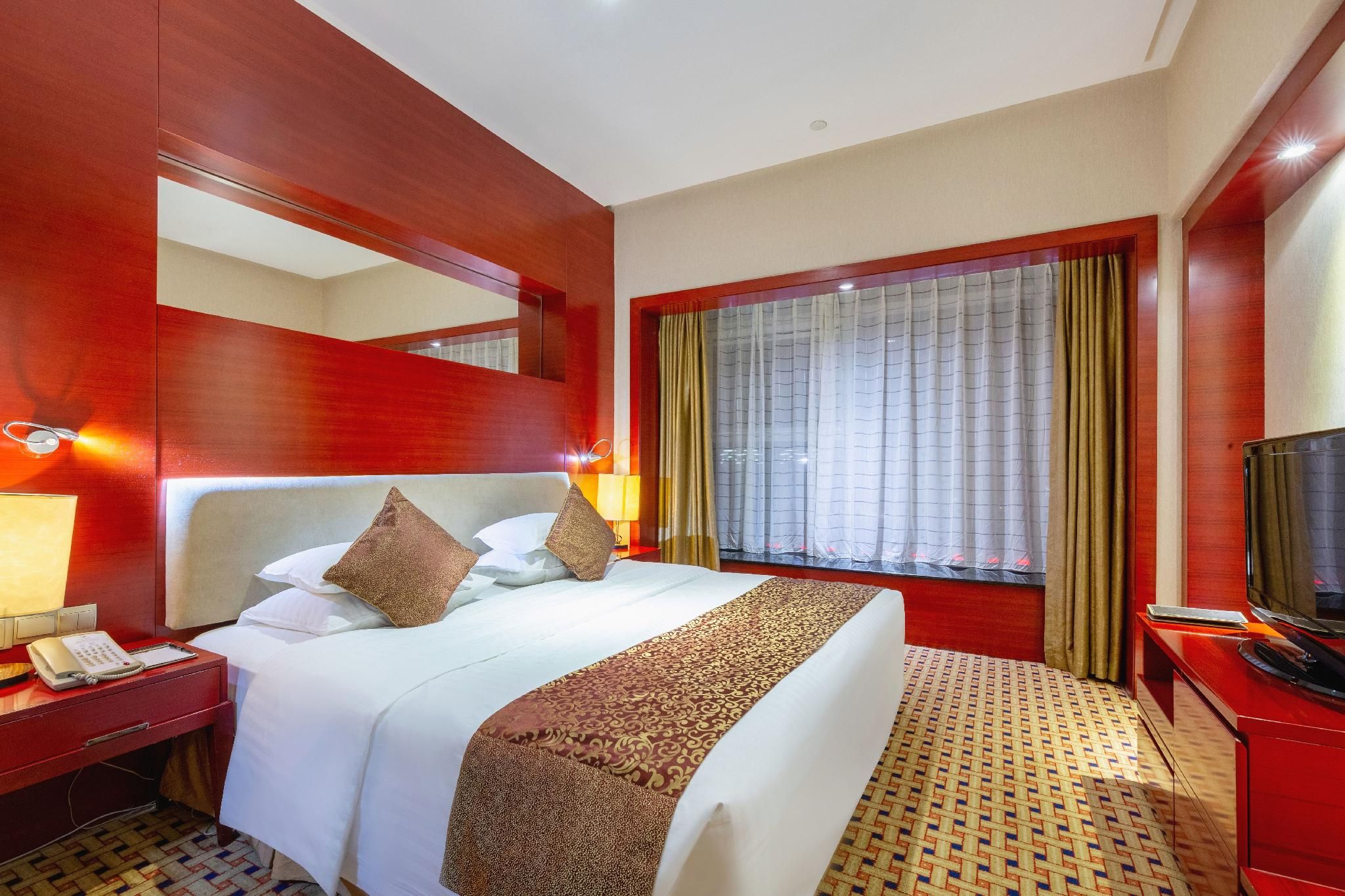 A hotel room with a large bed, a bedside table with a phone, a TV, and a window with curtains.