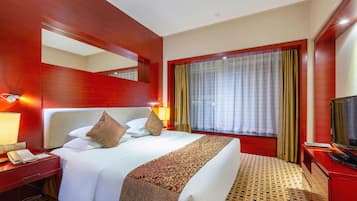 A hotel room with a large bed, a bedside table with a phone, a TV, and a window with curtains.