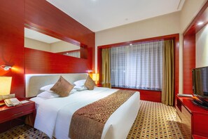 A hotel room with a large bed, a bedside table with a phone, a TV, and a window with curtains.